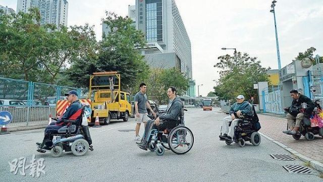自强协会属下四轮社区联会的成员庄先生（左起）、黄炳伸、阿本及庆文上周试行从颂富站到天水围医院（图中）的路段，从天瑞路转入天坛街需过马路，其间需闪避左右驶来以及于露天停车场出入的车辆。