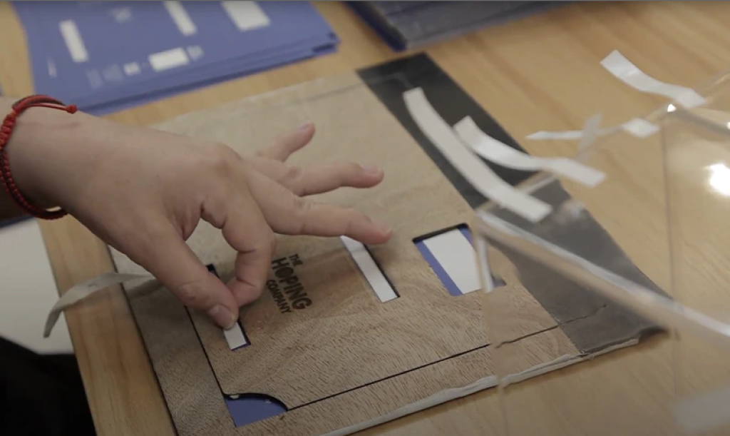 Jason便設計了一塊簡單的定位板，在木板上開出要貼貼的空位，只要把貼紙貼在空位上，便能確保正確，不用再慢慢用眼睛和手對位。